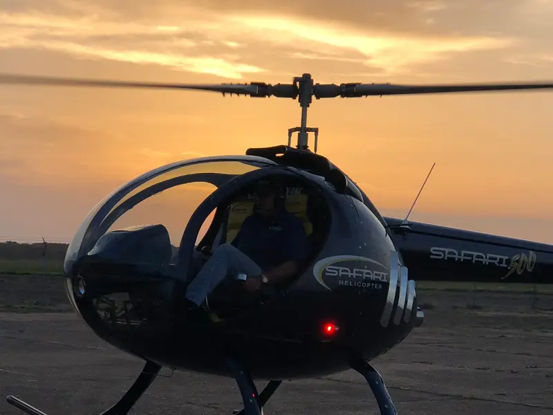 Safari 500 helicopter with enclosed carbon-fiber cabin and SAFARI script on the ground at sunset, low front three-quarter view