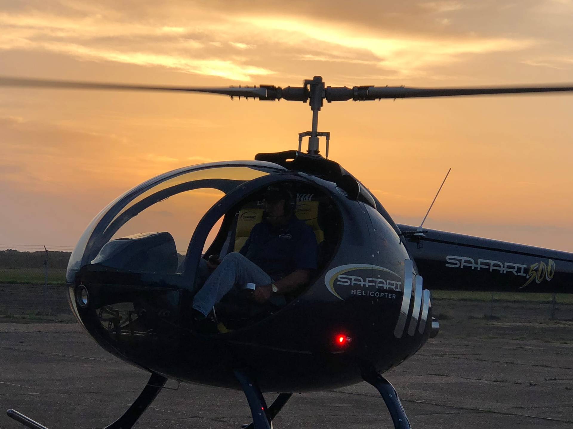 Safari 500 helicopter with enclosed carbon-fiber cabin and SAFARI script on the ground at sunset, low front three-quarter view