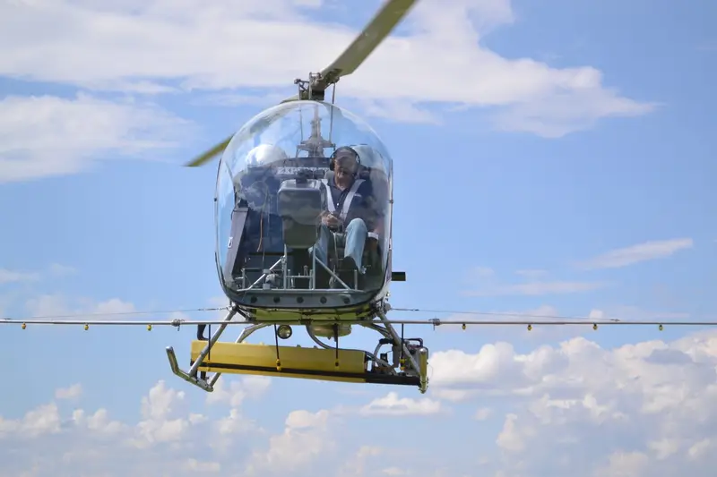 Safari 400 helicopter with yellow skid-mounted fuel tanks hovering under a clear blue sky