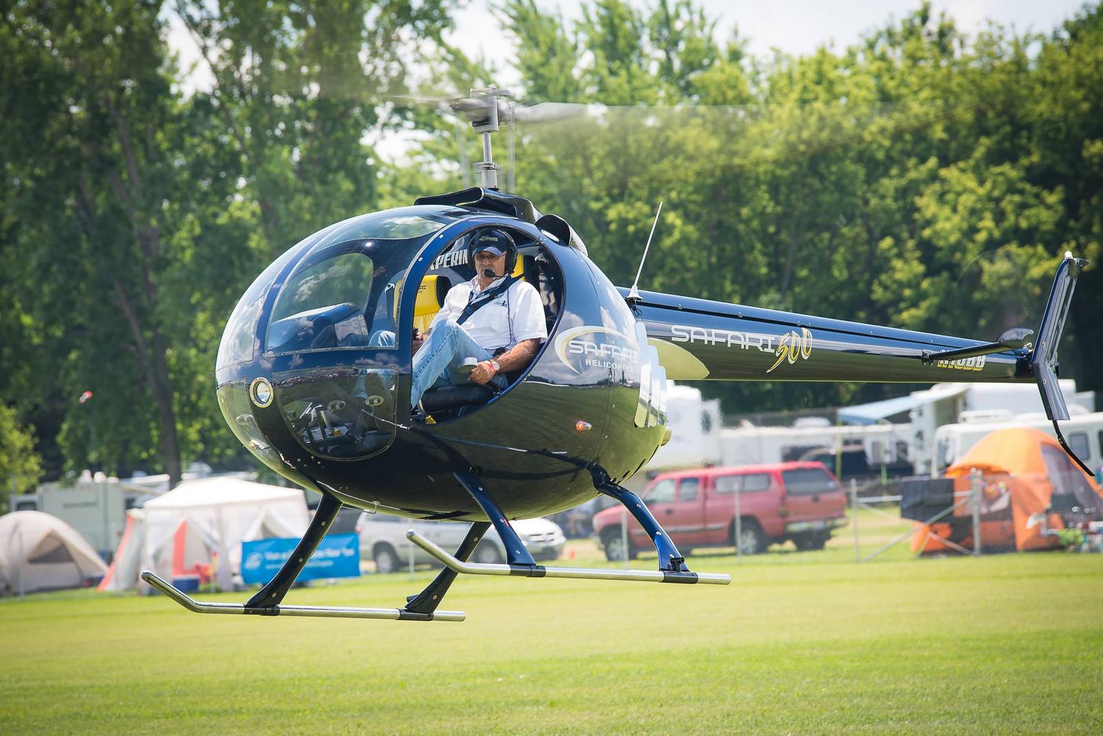 Black Safari 500 helicopter on grass at a fly-in with the pilot aboard, front three-quarter view