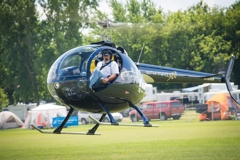 Black Safari 500 helicopter on grass at a fly-in with the pilot aboard, front three-quarter view